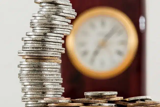 Bank fees show by stacking up in coins with a clock behind it
